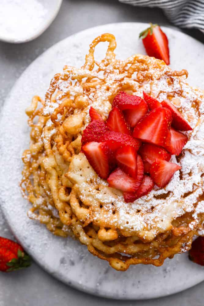 Skip the fair and make your own funnel cake at home! The batter is so quick and easy, you only need 20 minutes to make this fun treat at home. It will feel like a night out and taste better than any funnel cake you've ever had. An overhead view of funnel cakes topped with straberries.