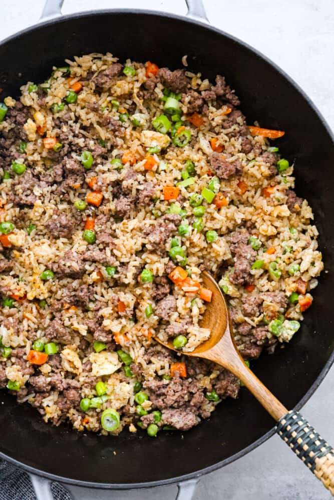 This easy Beef Fried Rice is ready in under 30 minutes and so delicious! It's a great way to reinvent leftover rice into a filling and satisfying meal that the whole family will love. With just a few simple ingredients, you'll find yourself making this recipe all the time! Beef fried rice in a pan with a wooden spoon sticking out of it.