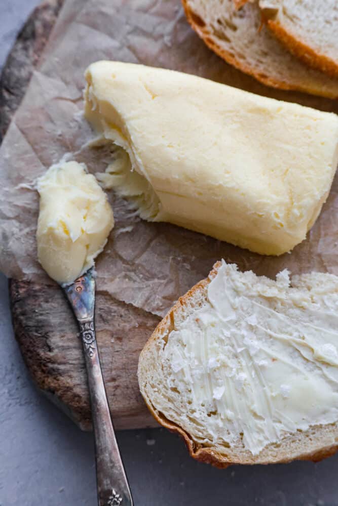 Storebought butter can be full of unnecessary and lower quality ingredients- make your own butter at home instead! You will be blown away by how flavorful and delicious this homemade butter is. Not to mention it's a really fun activity for the whole family too! An overhead view of homemade butter and some spread on a piece of bread.