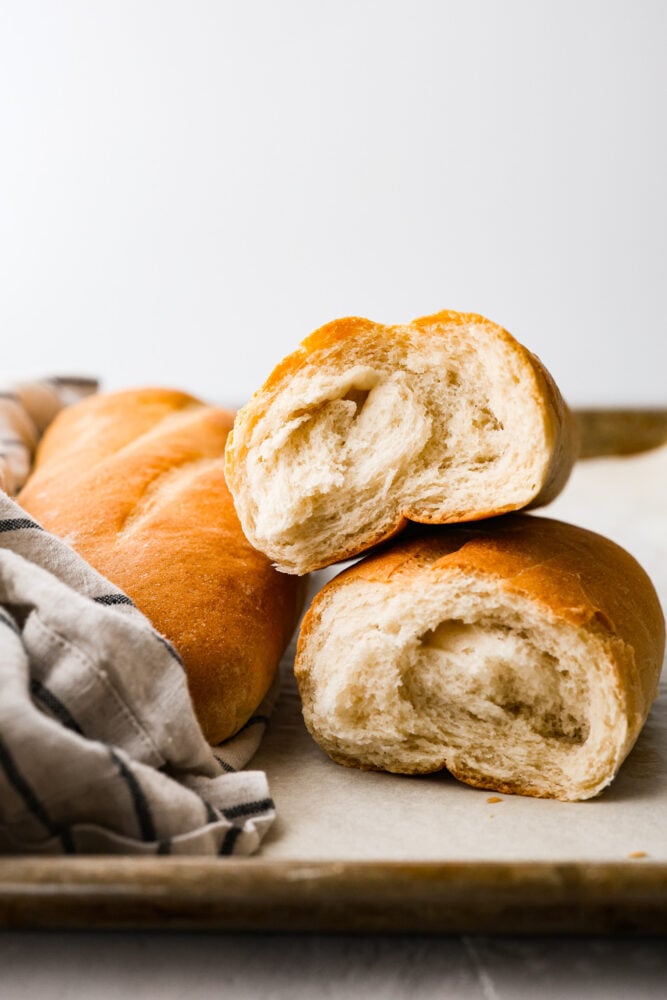 Skip the bakery and make your own artisan Italian bread at home! This bread is perfect for subs and sandwiches of every kind. Besides, no one can resist the smell of fresh bread hot out of the oven! Italian bread ripped in half and stacked on top of each other showing the fluffy inside.