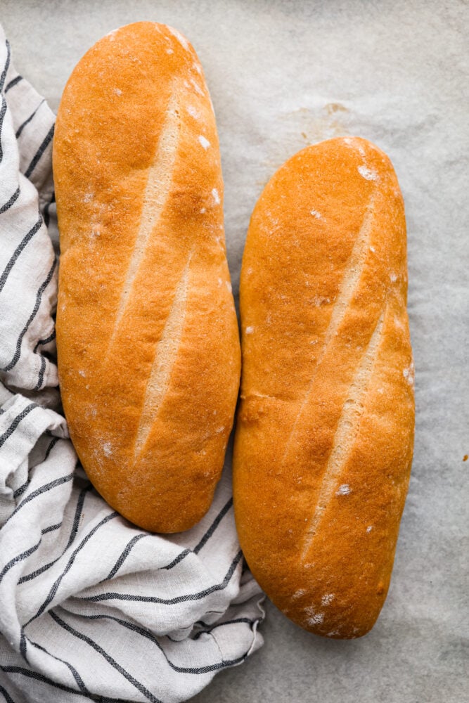 Skip the bakery and make your own artisan Italian bread at home! This bread is perfect for subs and sandwiches of every kind. Besides, no one can resist the smell of fresh bread hot out of the oven! An overhead view of two loaves of Italian bread.
