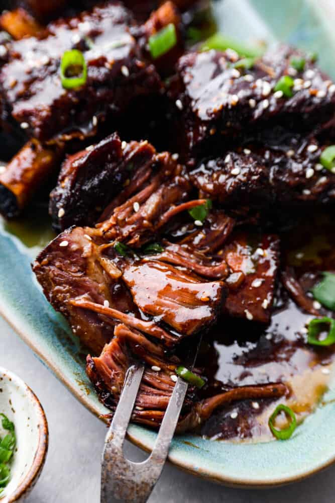 These bone-in Korean short ribs are sticky savory perfection! This recipe is as simple as searing your ribs and tossing them in a marinade and into the crock pot. The result is tender and flavorful meat that will have you coming back for seconds and thirds! A close up on the Korean short ribs on the platter being pulled apart.