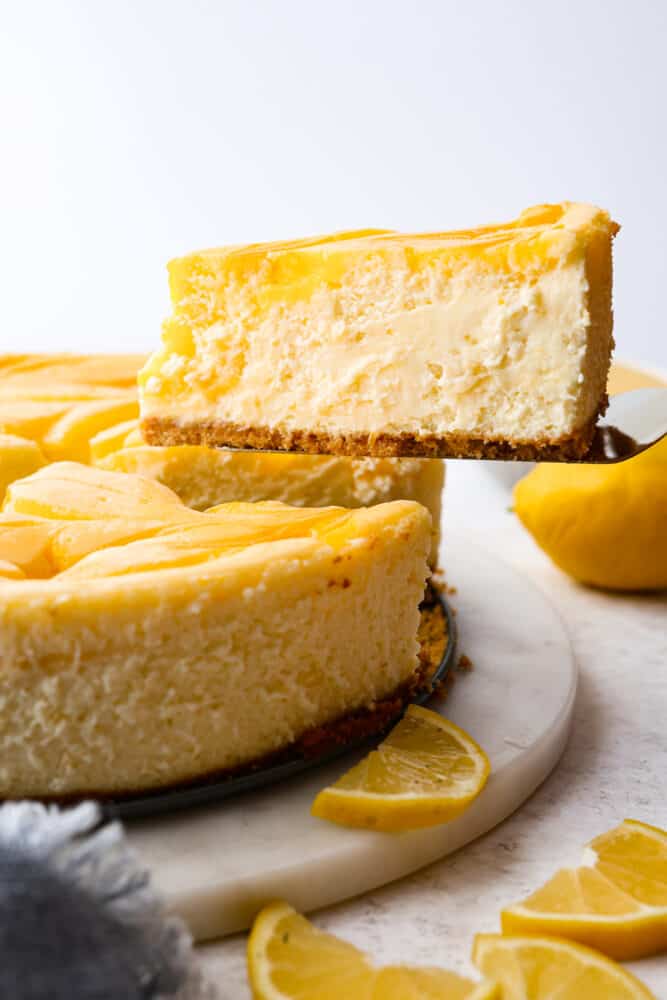 Trust me, you need this dreamy lemon cheesecake in your life. The lemon curd adds the perfect tangy kick to the creamy cheesecake filling, making every bite a smooth, heavenly experience. One slice just won't cut it, you'll want to indulge in the whole cake! A slice being served with a cake spatula.
