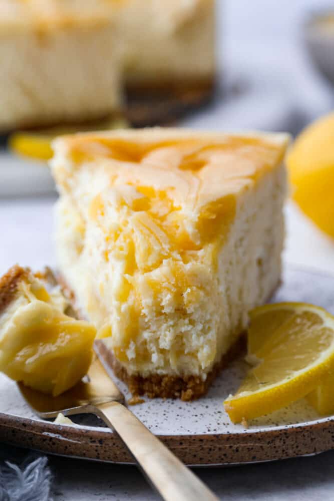 Trust me, you need this dreamy lemon cheesecake in your life. The lemon curd adds the perfect tangy kick to the creamy cheesecake filling, making every bite a smooth, heavenly experience. One slice just won't cut it, you'll want to indulge in the whole cake! Front view of a slice of lemon cheesecake.