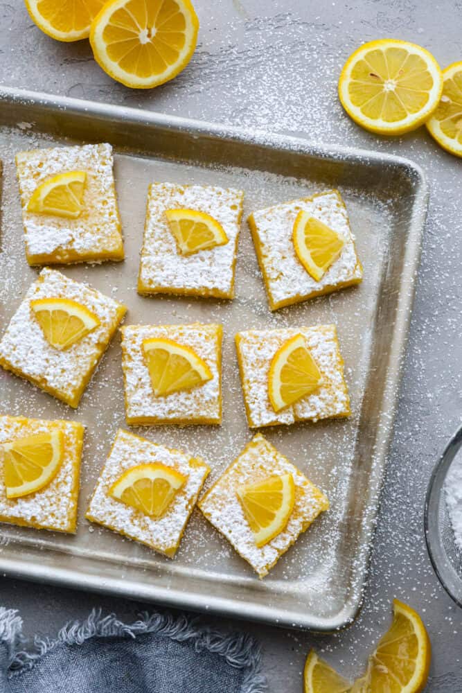 There’s nothing better than a buttery shortbread crust topped with a juicy lemon filling and a sprinkling of powder sugar. This classic recipe for lemon bars is the only one you’ll ever need! It’s happiness in bite-sized pieces. Top-down view of lemon bars in a baking sheet.