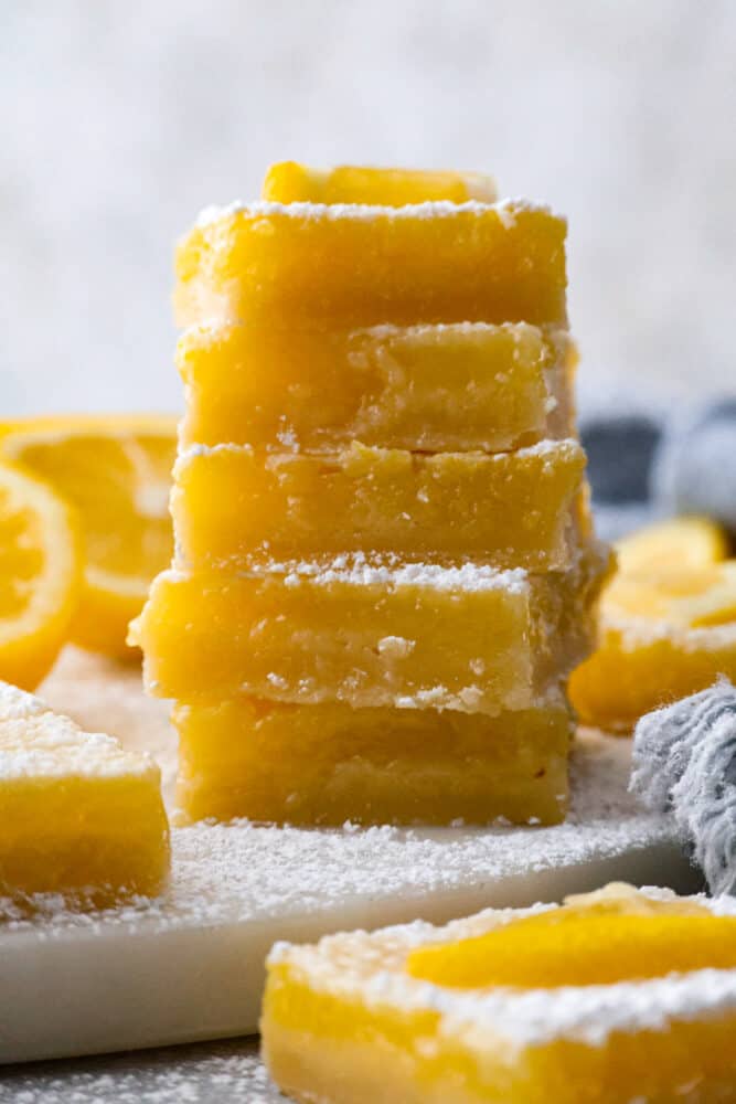 There’s nothing better than a buttery shortbread crust topped with a juicy lemon filling and a sprinkling of powder sugar. This classic recipe for lemon bars is the only one you’ll ever need! It’s happiness in bite-sized pieces. 5 lemon bar squares stacked on top of each other.