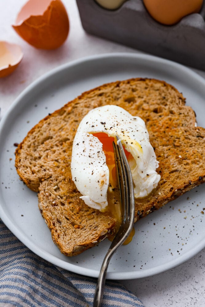 Soft egg whites and warm runny yolks are reason enough for every home chef to know how to poach an egg! It's not as hard as it sounds, and these eggs are so next level you won't believe what you've been missing out on all these years! A poached egg being cut open on top of a piece of toast by a fork.