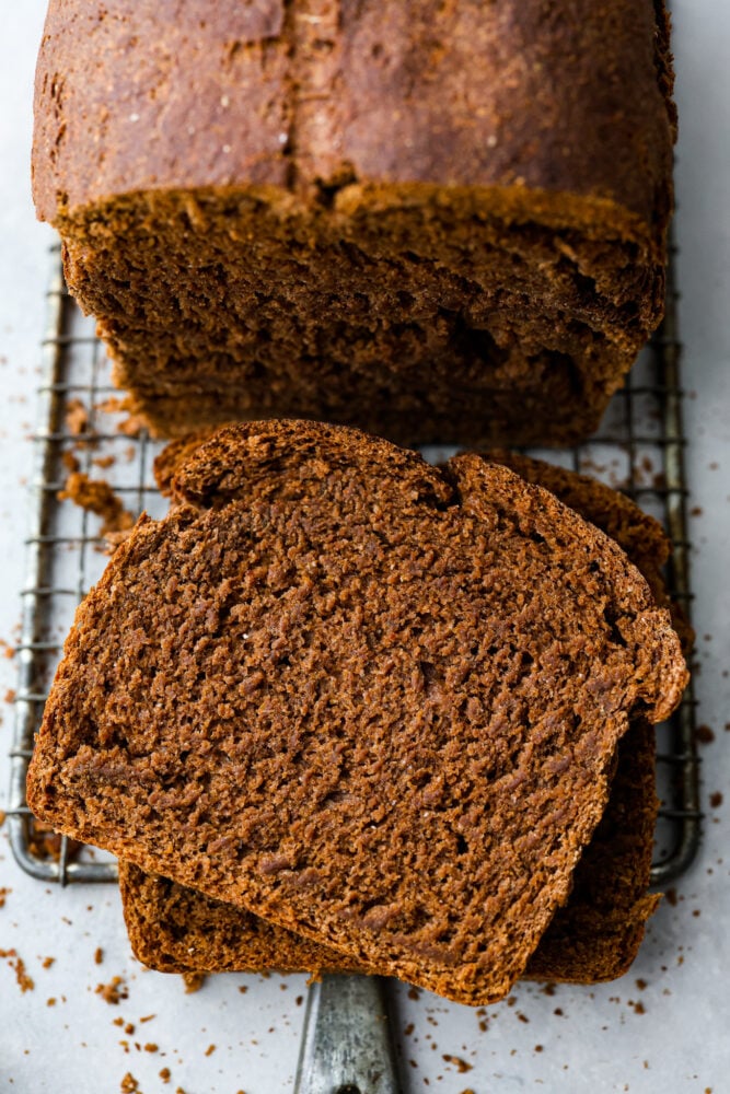 This pumpernickel bread is full of rich and hearty flavor. With three types of flour and brown sugar and molasses, you won't believe how much you can enjoy this nutrient-rich bread! To top it all off, it has cocoa powder to take things to a whole other level. An overhead look at the loaf of pumpernickel bread with a few slices cut off on top of a wire rack.