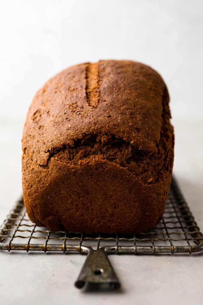 This pumpernickel bread is full of rich and hearty flavor. With three types of flour and brown sugar and molasses, you won't believe how much you can enjoy this nutrient-rich bread! To top it all off, it has cocoa powder to take things to a whole other level. A side view of the loaf of pumpernickel bread on a wire rack.