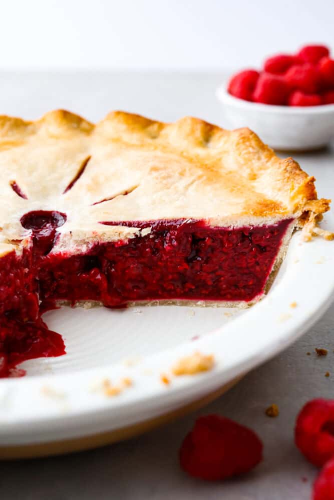 Raspberry pie is a timeless dessert that has been enjoyed for generations, and for good reason. With its flaky, buttery crust and tangy-sweet filling bursting with fresh, juicy raspberries, it’s the perfect balance of flavors and textures. And while store-bought options are convenient, nothing beats making it from scratch! A whole pie cut into so the filling can be seen.