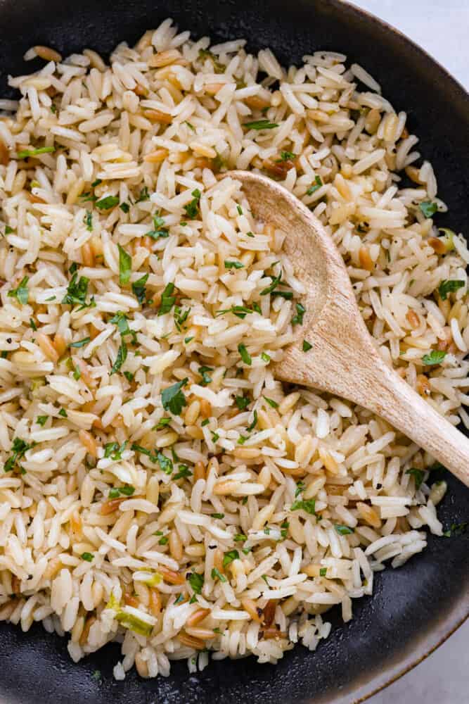 The combination of tender rice, toasty orzo, savory chicken broth, and aromatic green onions creates a mouth-watering medley that will have you coming back for seconds (and maybe even thirds!). Trust me, this rice pilaf will become a staple side dish in your kitchen once you give it a try. It's perfect for pairing with all of your favorite meals! Closeup of pilaf in a black bowl.