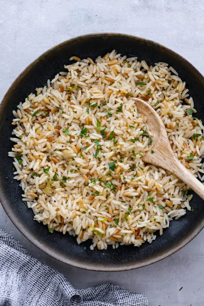 The combination of tender rice, toasty orzo, savory chicken broth, and aromatic green onions creates a mouth-watering medley that will have you coming back for seconds (and maybe even thirds!). Trust me, this rice pilaf will become a staple side dish in your kitchen once you give it a try. It's perfect for pairing with all of your favorite meals! Top-down view of rice pilaf served in a black bowl.