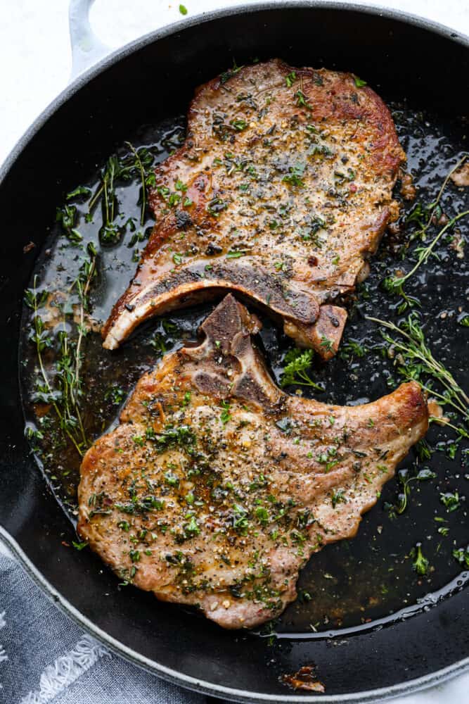 Cast Iron Skillet Pork Chops are a quick and delicious way to serve a satisfying gourmet meal. Bone in pork chops are coated with a garlic herb mixture and seared in a seasoned cast iron skillet for the juiciest and most flavorful pork chop you've ever had! Cast iron skillet pork chops in a cast iron pan.