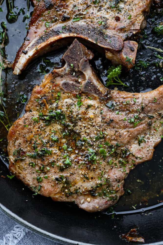 Cast Iron Skillet Pork Chops are a quick and delicious way to serve a satisfying gourmet meal. Bone in pork chops are coated with a garlic herb mixture and seared in a seasoned cast iron skillet for the juiciest and most flavorful pork chop you've ever had! A close up on the skillet pork chops.