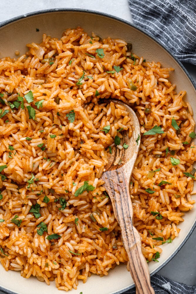 This Spanish rice delivers warm and exciting flavors that complement any meal! This tastes just like your favorite restaurant rice and is delicious served with any protein or Spanish inspired dish. A close up of the Spanish rice in the skillet with a wooden spoon.