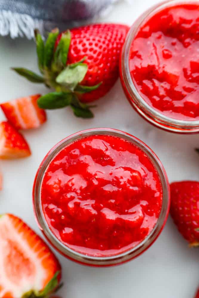 This quick and easy recipe for Homemade Strawberry Sauce is a must-have! This is a great way to use up fresh summer strawberries or to keep the ones you have in the fridge from going bad. I include plenty of tips for making your sauce thinner or thicker and glossier, too! An overhead view of strawberry sauce in a jar.