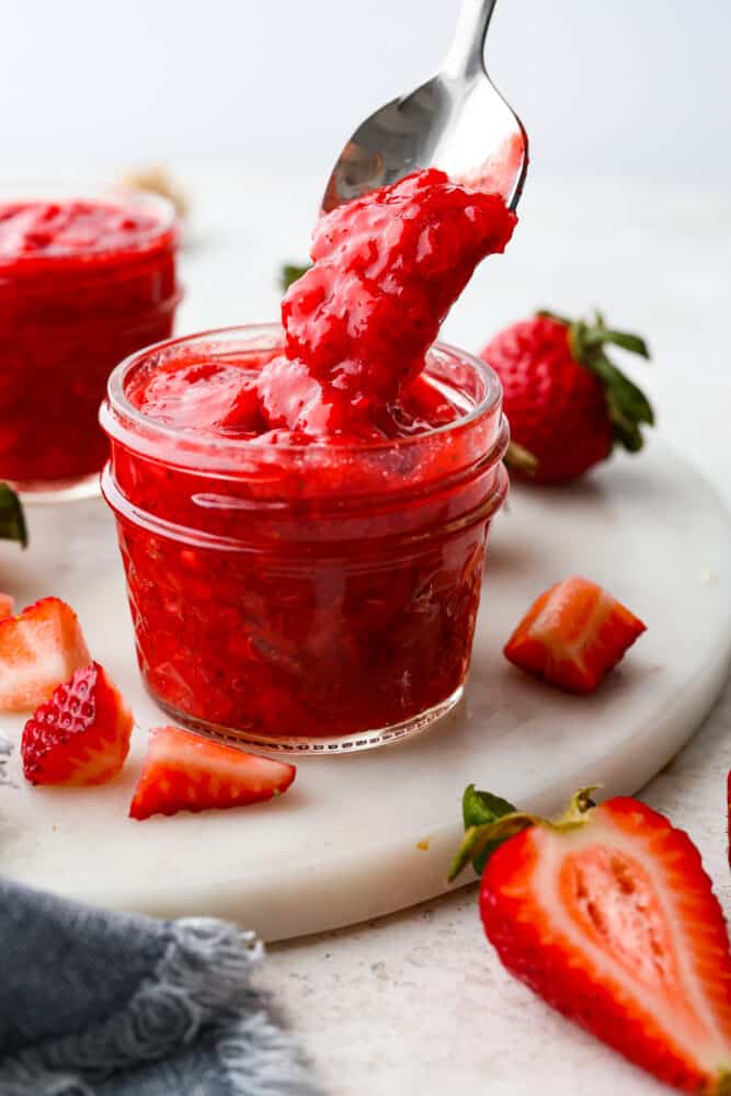 This quick and easy recipe for Homemade Strawberry Sauce is a must-have! This is a great way to use up fresh summer strawberries or to keep the ones you have in the fridge from going bad. I include plenty of tips for making your sauce thinner or thicker and glossier, too! Strawberry sauce in a jar with a spoon taking some out.