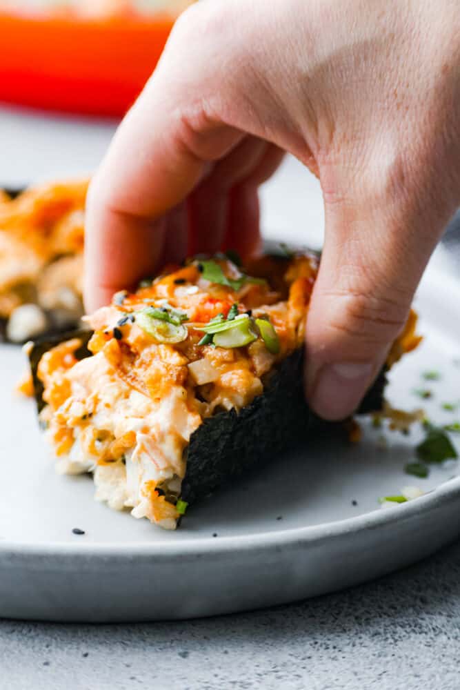 This sushi bake is a deconstructed California sushi roll that is packed with flavor and all of your favorite sushi ingredients. It's layers of delicious fish, sushi rice, and the best blend of seasonings. It's an easy layered dish that is absolutely addicting! A hand wrapping nori around the sushi bake.