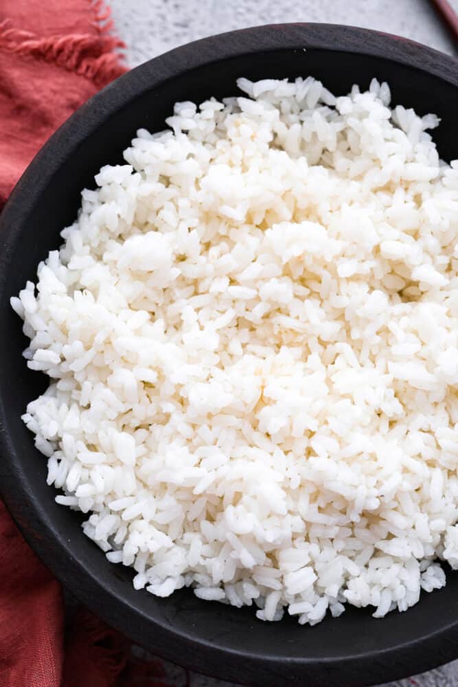 If you are obsessed with sushi like I am, it's time you learned to make Sushi Rice at home! It's so sticky and delicious, and easier than you may think. Impress your friends with a sushi night in! A close up of sushi rice in a bowl.