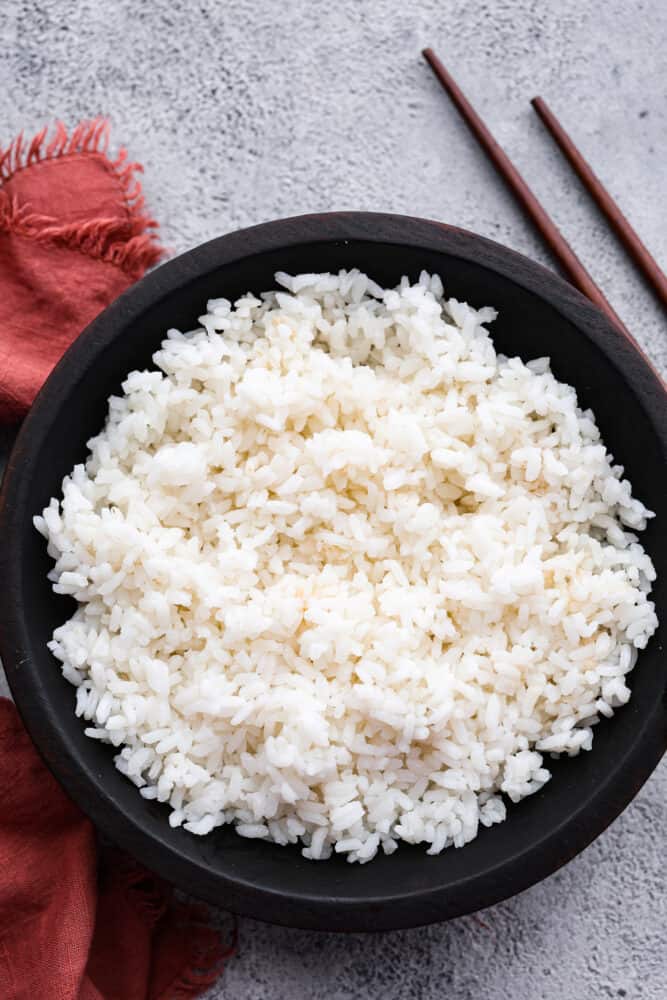 If you are obsessed with sushi like I am, it's time you learned to make Sushi Rice at home! It's so sticky and delicious, and easier than you may think. Impress your friends with a sushi night in! Sushi rice in a black bowl.