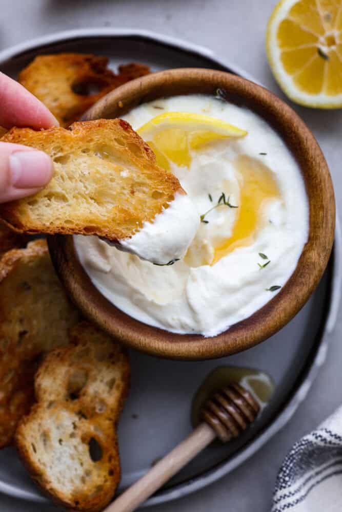 This whipped ricotta made with lemon, honey, and fresh herbs is going to be your new favorite dip. (It also doubles as a spread!) It's light and creamy, but so flavorful! Serve it up with your favorite pita chips and you have an appetizer that's perfect for enjoying all spring and summer long. Dipping a slice of baguette in the whipped ricotta.