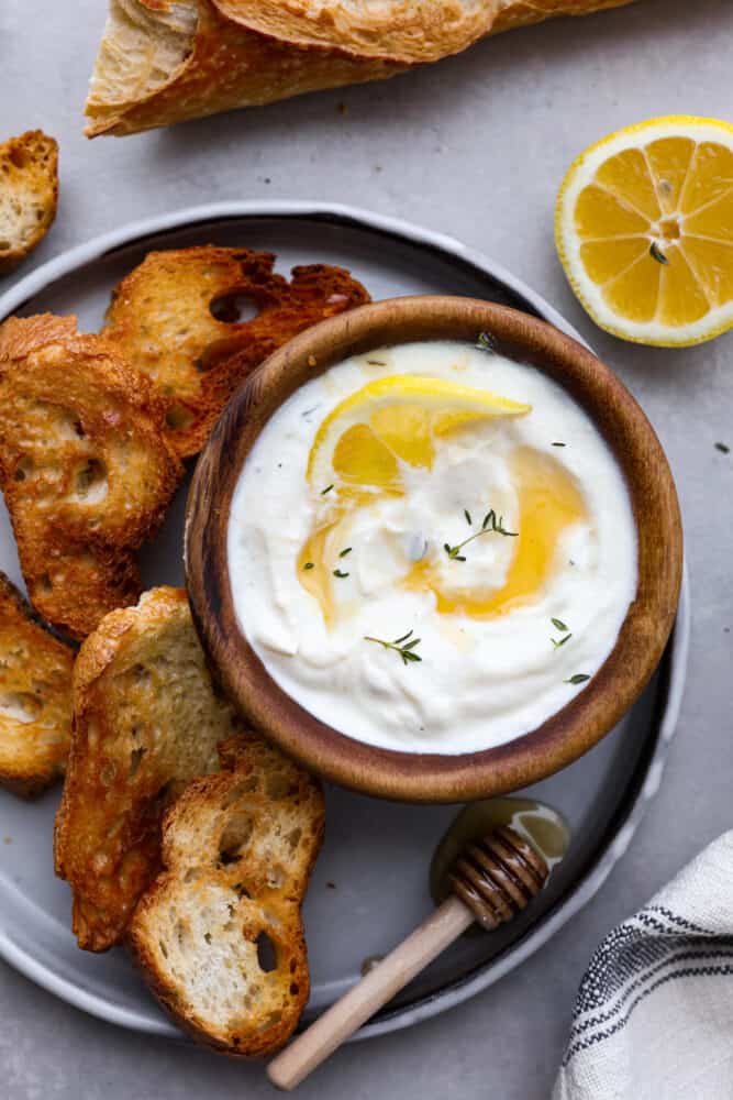 This whipped ricotta made with lemon, honey, and fresh herbs is going to be your new favorite dip. (It also doubles as a spread!) It's light and creamy, but so flavorful! Serve it up with your favorite pita chips and you have an appetizer that's perfect for enjoying all spring and summer long. A small bowl of whipped ricotta served with baked slices of baguette.