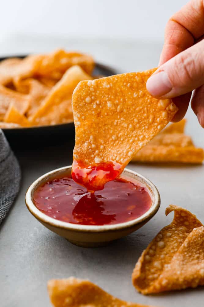 Get ready to up your snack game, because I've got a game-changing recipe for you: wonton chips are where it's at! These golden, crispy triangles are the perfect vessel for all your favorite dips, from guacamole to hummus to sweet and sour sauce. Once you get a taste of that heavenly crunch, you'll wonder how you ever lived without them. Dipping a chip into sweet and sour sauce.