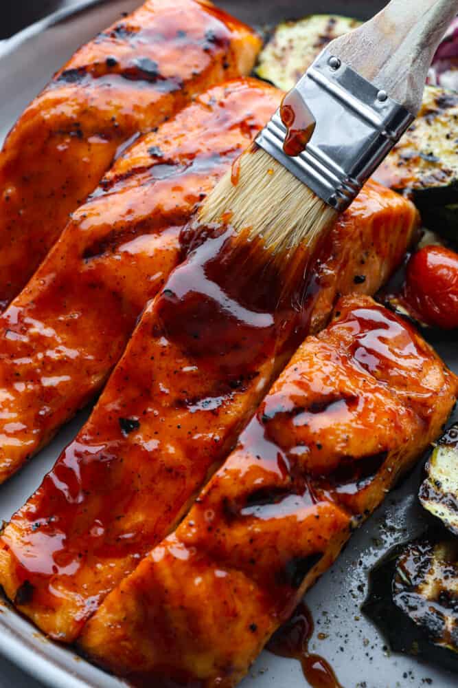 You guys know I'm obsessed with salmon! This BBQ salmon is perfectly smoky, tender, and coated in my mouthwatering homemade barbecue sauce. Someone spreading BBQ sauce on the salmon.