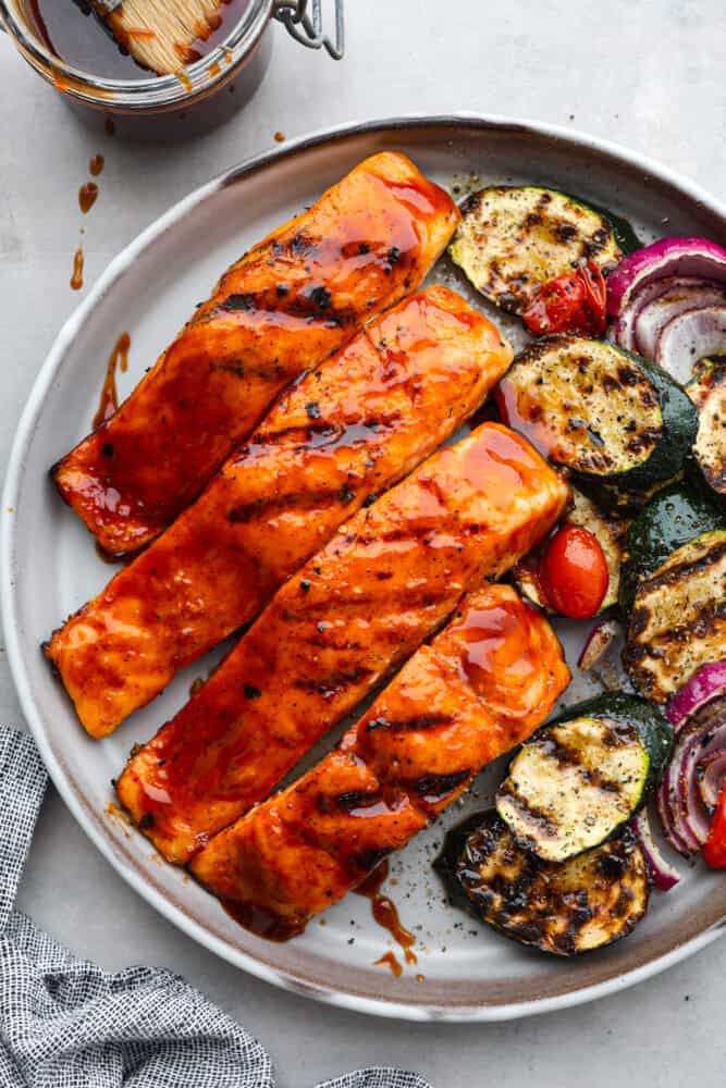 You guys know I'm obsessed with salmon! This BBQ salmon is perfectly smoky, tender, and coated in my mouthwatering homemade barbecue sauce. Top-down view of BBQ salmon on a white plate served with roasted zucchini.