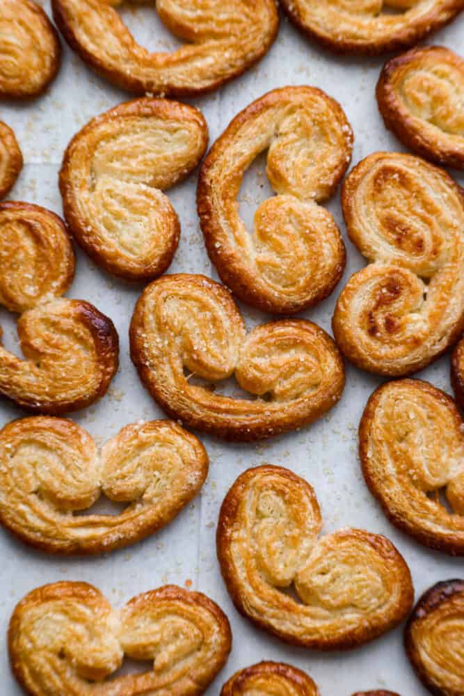 Palmiers, or "palm trees" in French, are a delightful pastry shaped like a palm leaf. With a buttery, flaky texture that's impossible to resist, enjoy one fresh out of the oven and prepare to be amazed. Top-down view of palmiers on parchment paper.