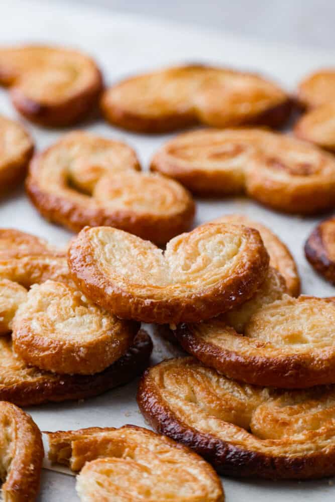 Palmiers, or "palm trees" in French, are a delightful pastry shaped like a palm leaf. With a buttery, flaky texture that's impossible to resist, enjoy one fresh out of the oven and prepare to be amazed. Hero image of palmier cookies.