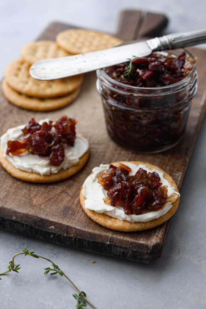 I know it may sound like an unusual combination, but trust me when I say bacon jam is a game-changer. This sweet and savory spread, made with crispy bacon, caramelized onions, and a touch of maple syrup, can elevate any dish from ordinary to extraordinary. It has a sweet and savory flavor that goes well with so many different foods, from toast and crackers to burgers and sandwiches. Bacon jam and cheese spread on 2 crackers.