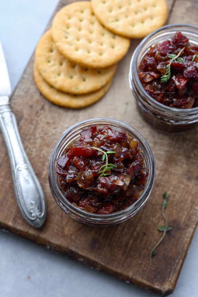 I know it may sound like an unusual combination, but trust me when I say bacon jam is a game-changer. This sweet and savory spread, made with crispy bacon, caramelized onions, and a touch of maple syrup, can elevate any dish from ordinary to extraordinary. It has a sweet and savory flavor that goes well with so many different foods, from toast and crackers to burgers and sandwiches. Top-down view of bacon jam in a glass jar on a wooden board served with crackers.