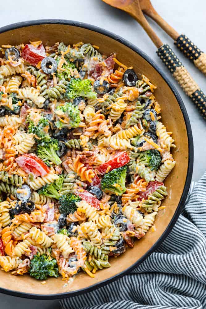This bacon ranch pasta salad is filled with colorful veggies and perfectly contrasting textures and flavors! Every bite is so satisfying it will be an incredible hit with anyone lucky enough to enjoy it! A bowl filled with bacon ranch pasta salad and 2 wooden spoons next to it.