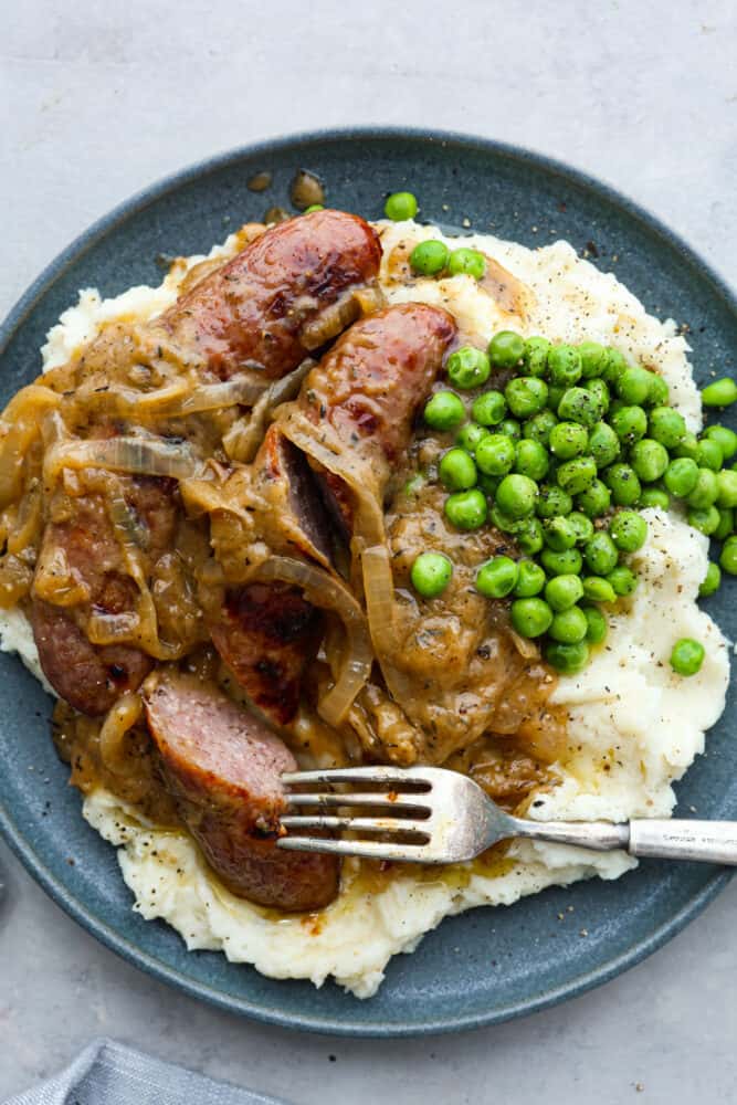 Bangers and mash, a classic British dish, is hearty comfort food at its finest! You'll love these fluffy mashed potatoes and flavorful pork sausages all smothered in a caramelized onion gravy. There's a reason why it's an English favorite! Taking a bite of a pork sausage.
