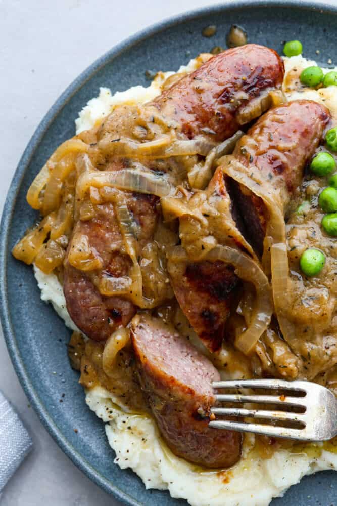 Bangers and mash, a classic British dish, is hearty comfort food at its finest! You'll love these fluffy mashed potatoes and flavorful pork sausages all smothered in a caramelized onion gravy. There's a reason why it's an English favorite! Closeup of bangers and mash.