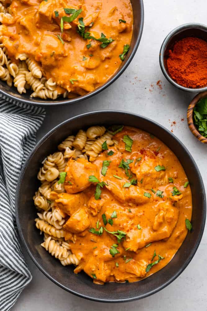 Indulge in a rich and creamy Chicken Paprikash that is so delicious, and it pairs perfectly over noodles. This classic Hungarian dish combines tender chicken with a flavorful blend of smoked paprika, onions, garlic, and tomatoes. The top view of 2 bowls filled with noodles and chicken paprikash.