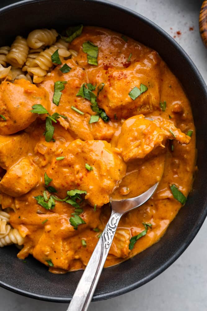 Indulge in a rich and creamy Chicken Paprikash that is so delicious, and it pairs perfectly over noodles. This classic Hungarian dish combines tender chicken with a flavorful blend of smoked paprika, onions, garlic, and tomatoes. the top view of chicken paprikash in a bowl with a silver spoon.