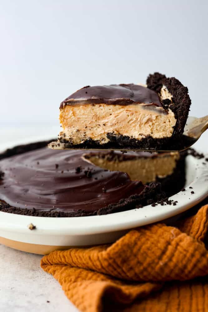 A fluffy, whipped peanut butter filling on top of an Oreo crust, all topped with chocolate ganache- what could be better than that? This chocolate peanut butter pie is the perfect dessert for anyone wanting something smooth, rich and indulgent! A slice of pie being served with a cake spatula.