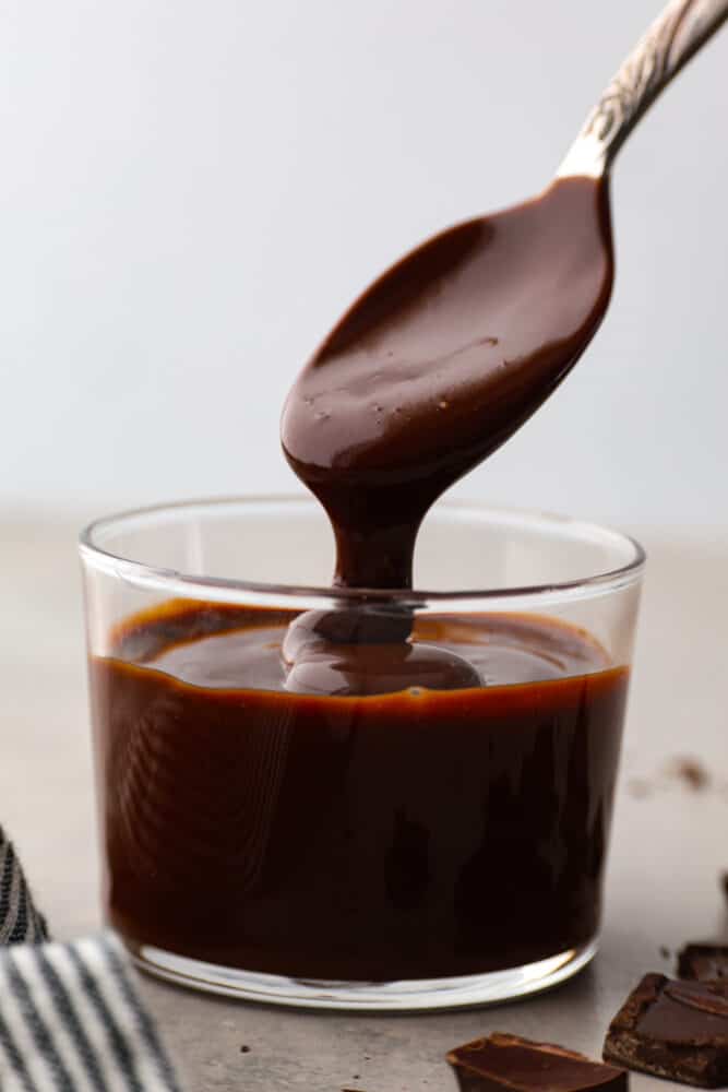 Everyone needs a great chocolate ganache recipe in their cookbook! This recipe is a classic and the best ganache recipe I've ever tried. It's perfectly shiny with rich chocolate flavor, and takes 5 minutes to whip up! Chocolate ganache in a glass container with a spoon taking a scoop out.