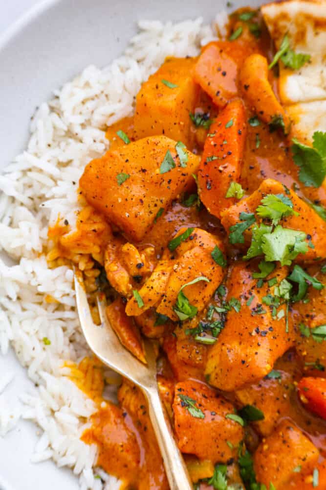 Coconut curry chicken is a mouthwatering dish that combines tender chicken, hearty vegetables, and a blend of aromatic spices, all simmered in a luscious coconut milk sauce. Serve it up with naan and basmati rice for a meal your family won’t be able to get enough of! Closeup of curry garnished with cilantro.