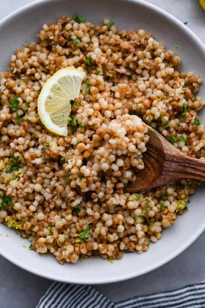 Looking to add a burst of Mediterranean flavor to your dining table? This delicious Israeli couscous is the answer! With its aromatic blend of olive oil, lemon zest, garlic, and fresh parsley, you won't be able to get enough. It's the perfect side dish for summer! Closeup of a spoonful of couscous.
