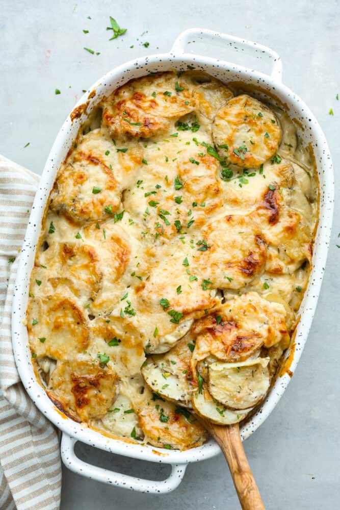 Scalloped potatoes are thinly sliced layered potatoes baked in a creamy garlic and herb sauce, making them tender and flavorful. Hearty and easy to make, this is the perfect side dish to any meal! Zoomed out shot of a pan of scalloped potatoes.
