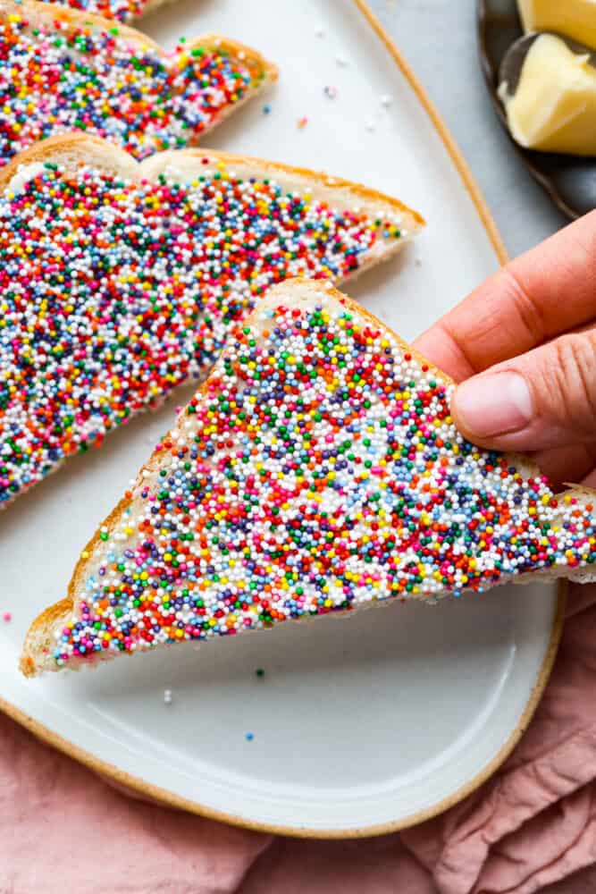 Fairy bread is the easiest treat to make and the best way to add a little magic to your day! These slices of buttery, sprinkled goodness are a classic Australian recipe, and sure to win your kids over. Closeup of a slice of fairy bread being picked up.