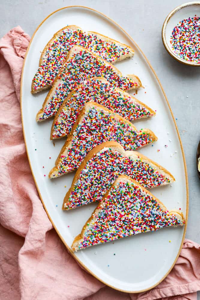 Fairy bread is the easiest treat to make and the best way to add a little magic to your day! These slices of buttery, sprinkled goodness are a classic Australian recipe, and sure to win your kids over. 6 slices of fairy bread on a white serving dish.