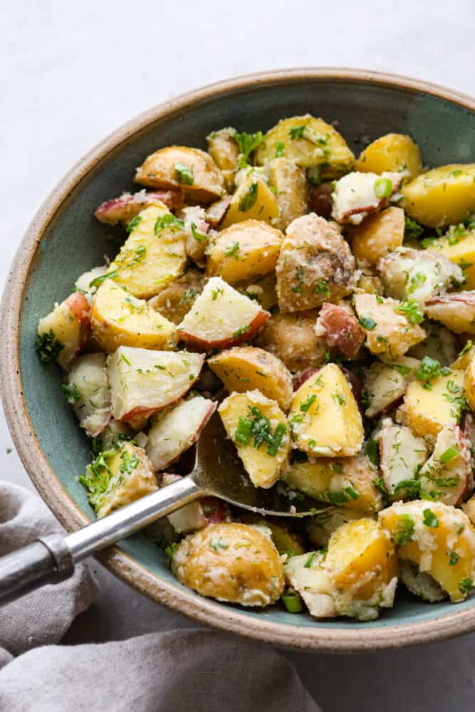 This French potato salad is a tasty mix of tender potatoes, green onions and herbs, all tossed in a zesty Dijon vinaigrette. The end result is a light and delicious side dish packed with bold flavor in every bite. Potato salad being served with a large metal spoon.