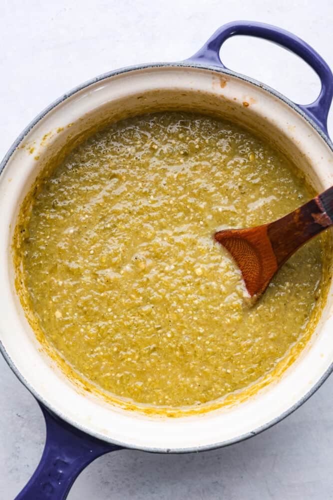 If you have some favorite enchiladas that are in need of a delicious sauce, look no more! This Homemade Green Enchilada Sauce is so delicious and packed with flavor. You will want to have it on hand all the time! A blue pot with a wooden spoon filled with cooked green enchilada sauce