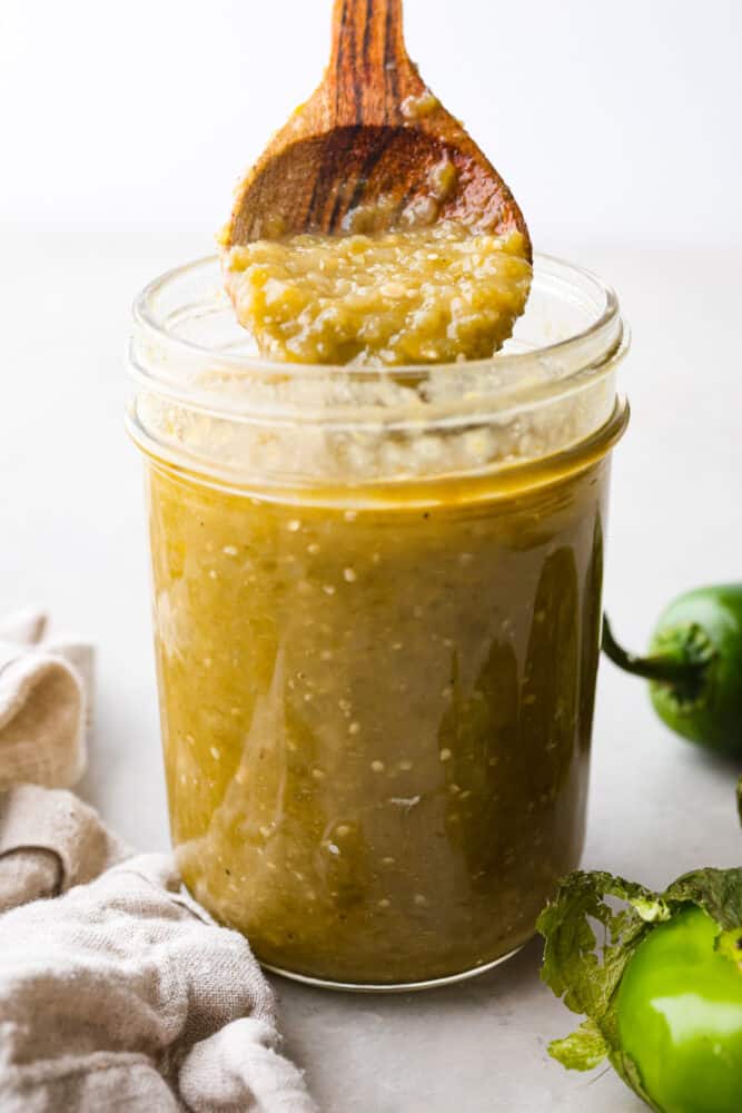 If you have some favorite enchiladas that are in need of a delicious sauce, look no more! This Homemade Green Enchilada Sauce is so delicious and packed with flavor. You will want to have it on hand all the time! A jar of homemade green enchilada sauce with a wooded spoon scooping some out.