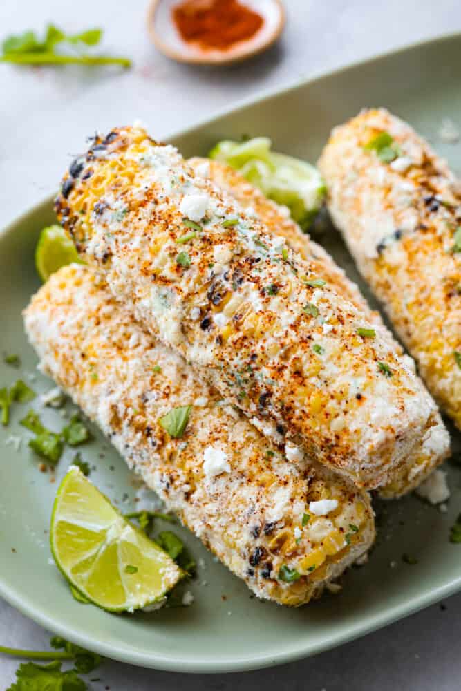 Grilled Mexican Street Corn is the perfect grilled corn slathered with an amazing mayonnaise blend and topped with parmesan cheese and chili powder. This is one of the best corn recipes you will eat! A close up of 4 Mexican grilled ears of corn on a green platter.