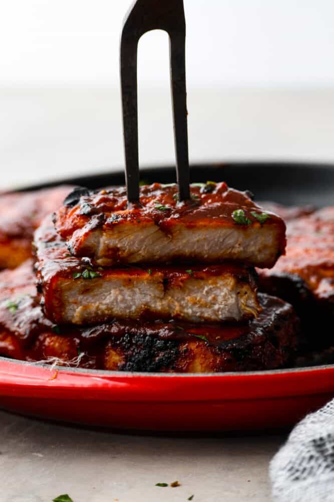 Get ready to take your pork chops to a whole new level with these BBQ Pork Chops. Grilled to perfection, they are juicy, tender, and bursting with tangy goodness. Prepare to impress your taste buds with this simple yet delicious dish. A sliced pork chop with a large carving fork holding the pieces together.